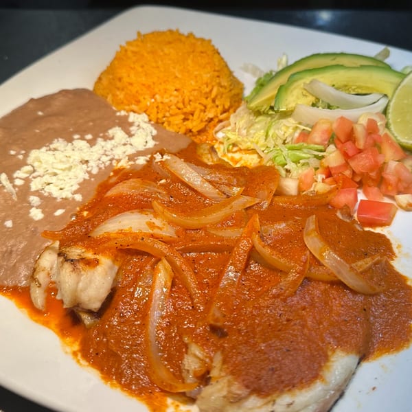 Mexican dish with fish in red sauce, onions, rice, refried beans, and salad with avocado.