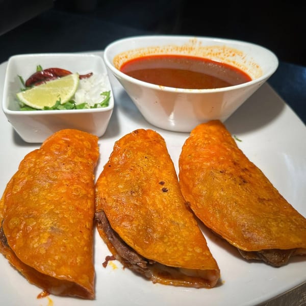 Three Javi Mexican Grill birria tacos with consommé and a side of lime, onions, and cilantro.