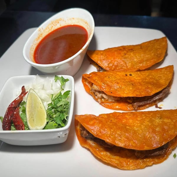 Three Javi Mexican Grill birria tacos with consommé, lime, cilantro, onions, and dried chilies.